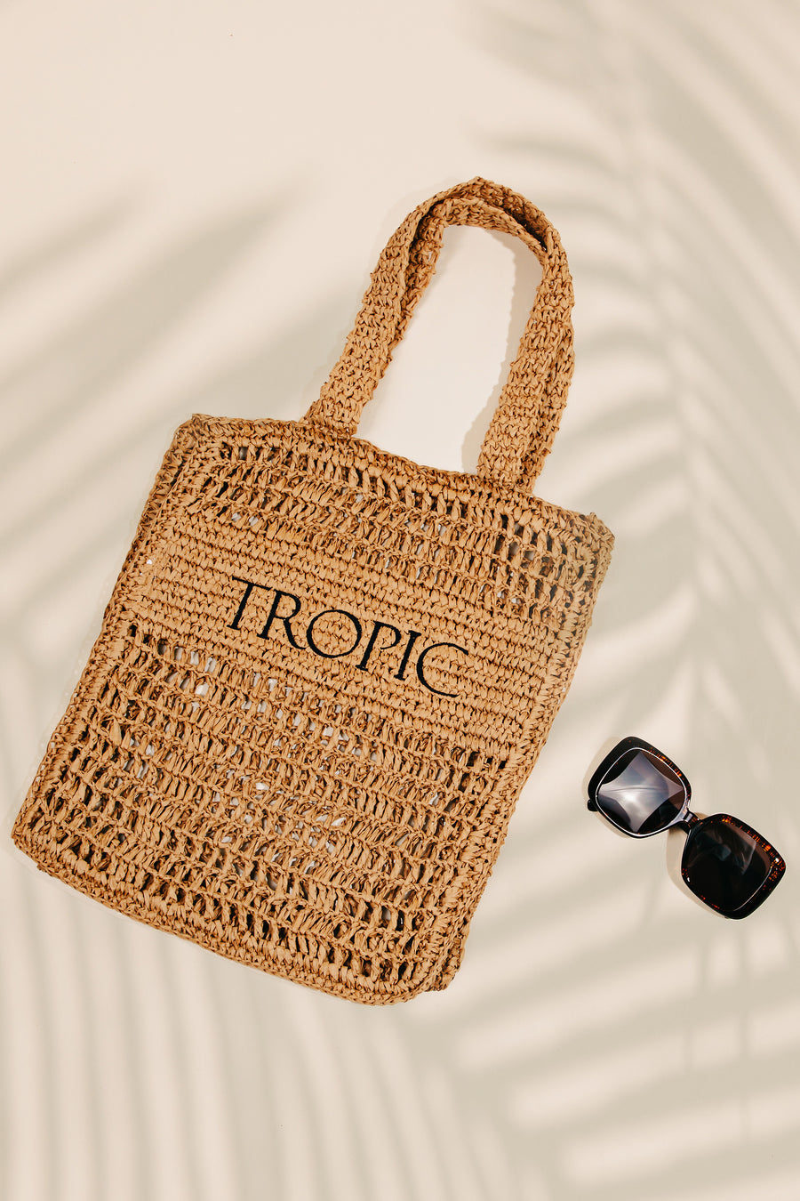 Featuring a woven shoulder bag in the color khaki with the word TROPIC printed on it 