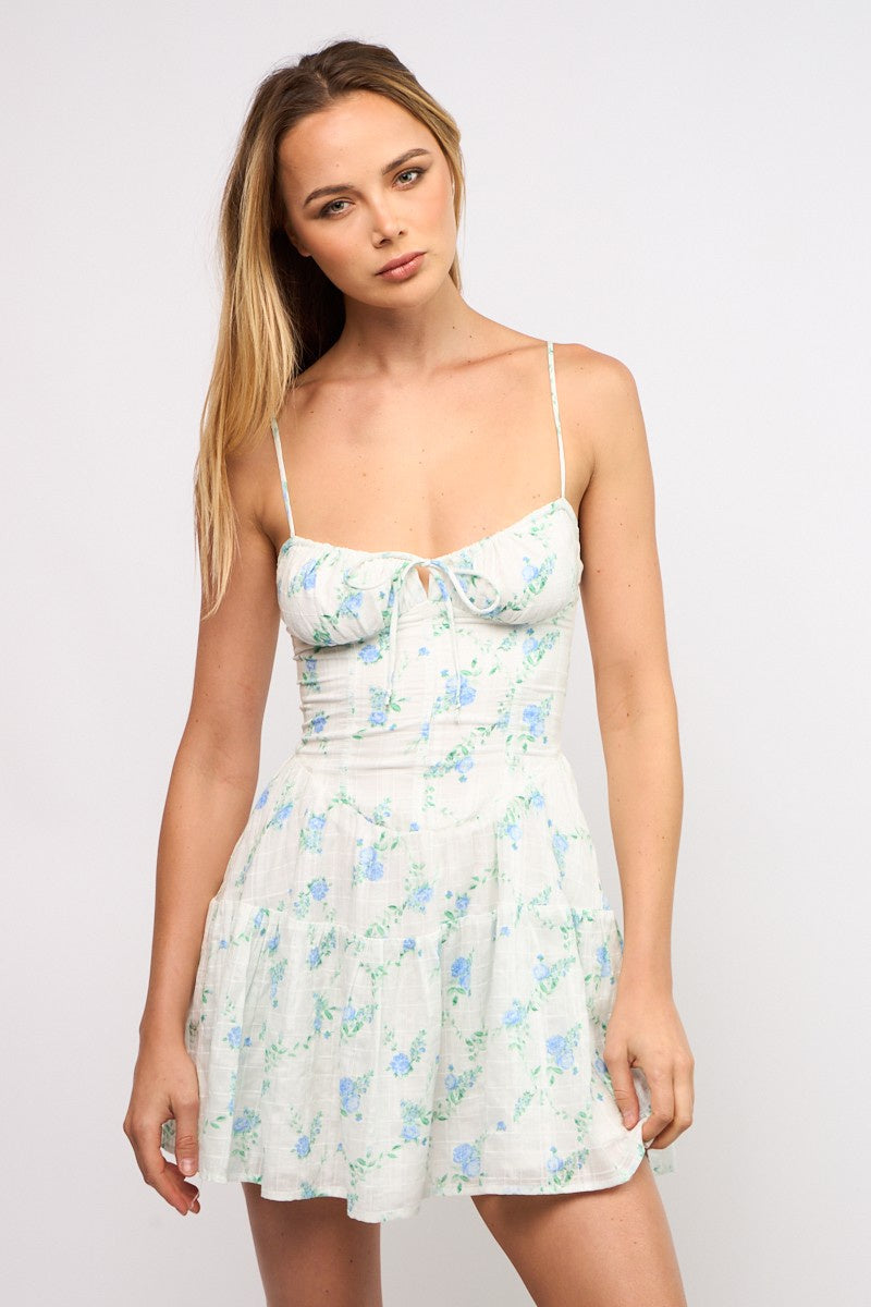 Featuring a floral mini dress with a corset shape, a front tie, back zipper and adjustable spaghetti straps in the color Blue Garden Floral with white background.