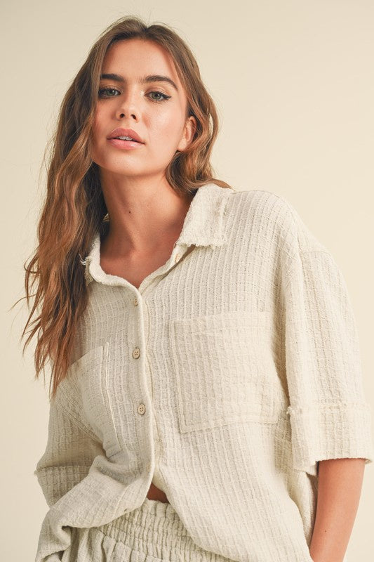 Featuring a textured gauze button up with rolled sleeves and two front chest pockets in the color oatmeal