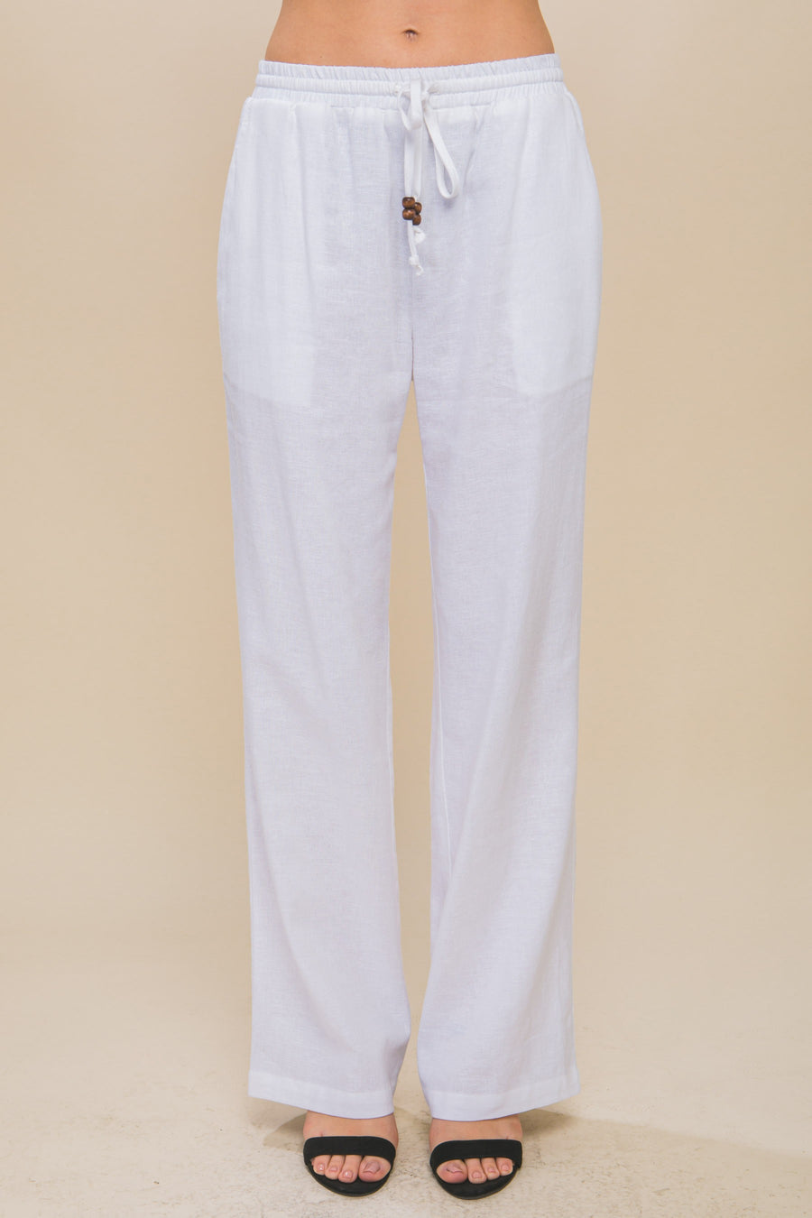 Featuring a straight leg linen pant with an elastic waist band and a tie front with added beaded detail in the color white 