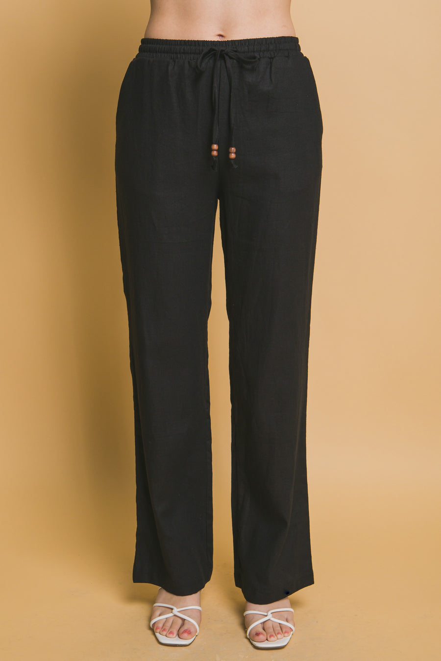 Featuring a straight leg linen pant with an elastic waist band and a tie front with added beaded detail in the color black