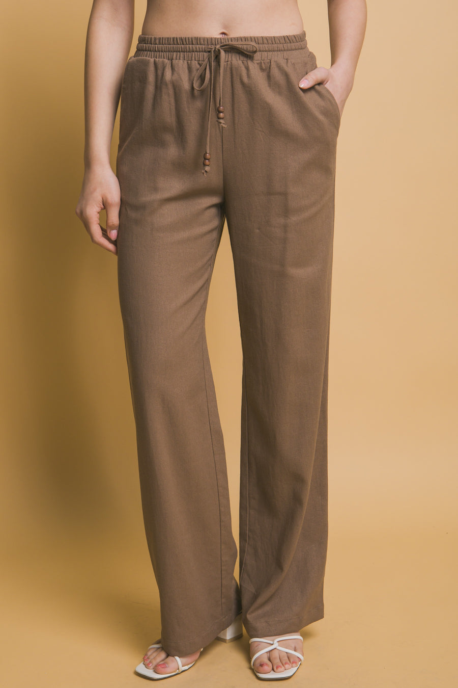 Featuring a straight leg linen pant with an elastic waist band and a tie front with added beaded detail in the color mocha 
