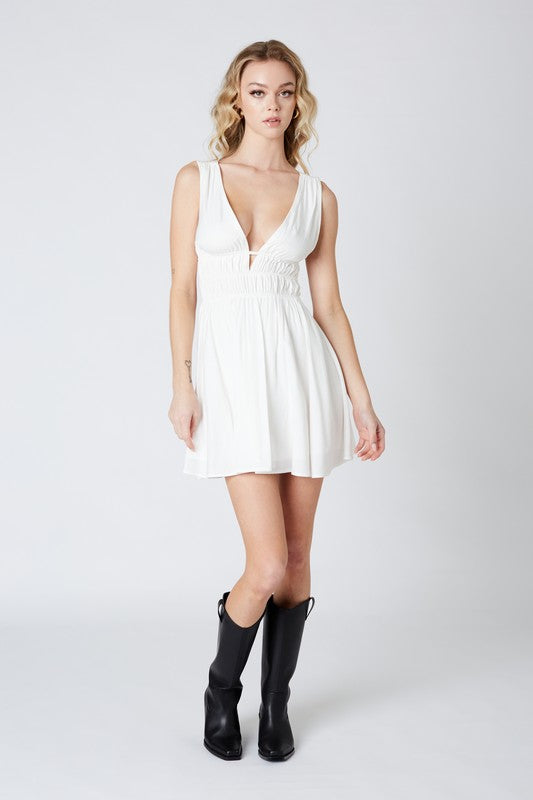 Featuring a deep v-neck mini dress with an open back and center ruching in the color white 