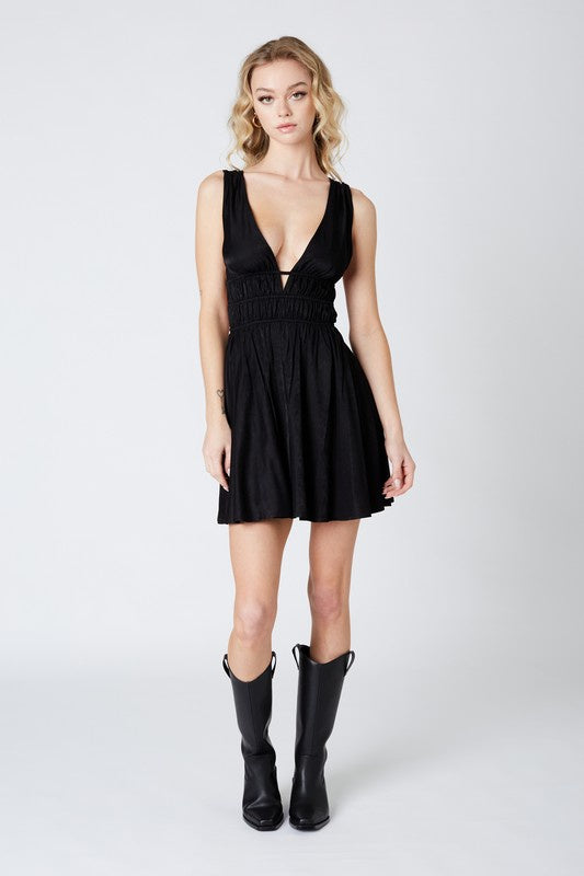 Featuring a deep v-neck mini dress with an open back and center ruching in the color black 