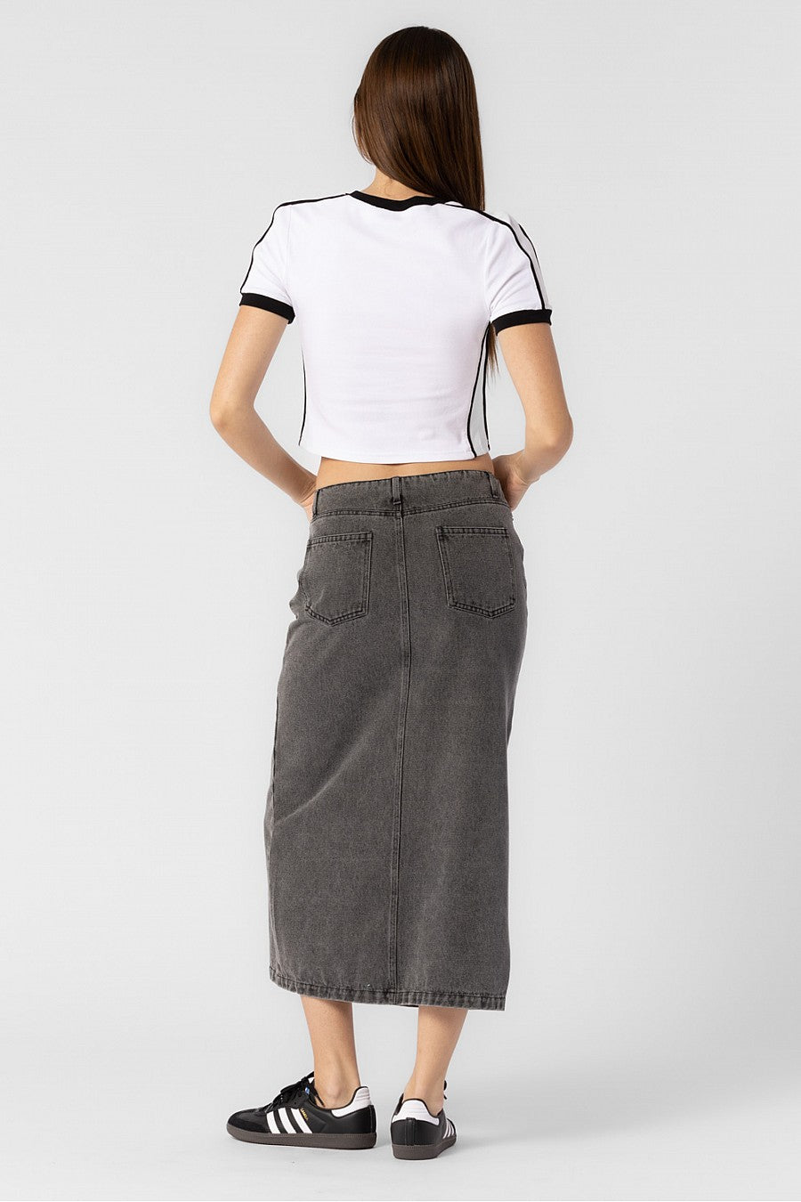 Model is wearing a grey denim midi skirt with front slit.