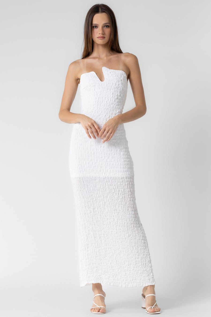 Featuring a white maxi dress with an asymmetrical strapless neckline and textured patterned fabric.