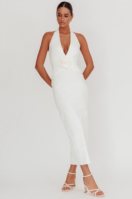 Featuring a halter deep V-neck maxi dress with a flower pin detail on the front in the color white 