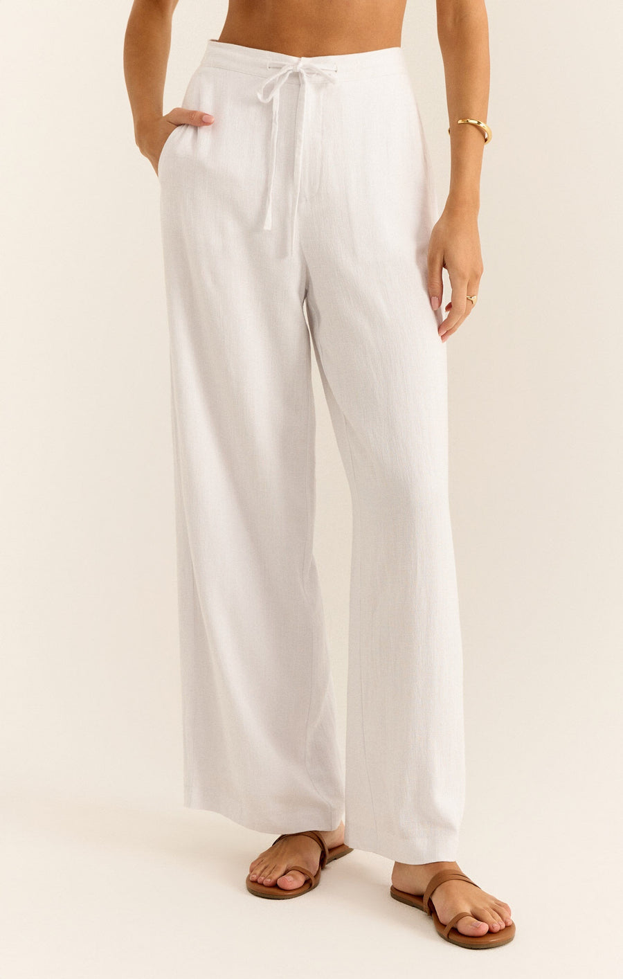 Featuring a wide leg linen pant with a zipper and button closure and a front tie detail in the color white 