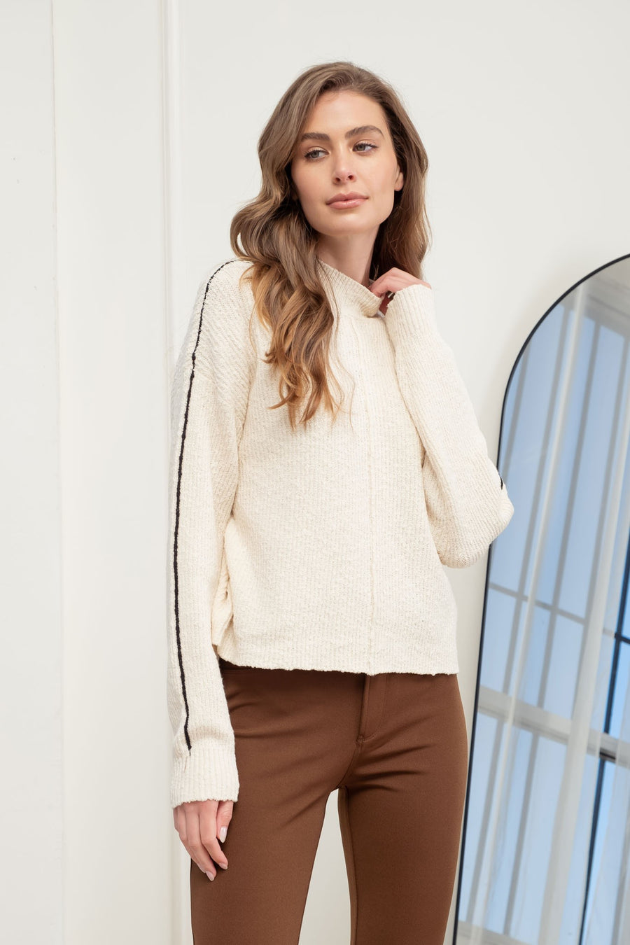 Featuring a mock neck knit sweater with contrast seams in the color oatmeal 