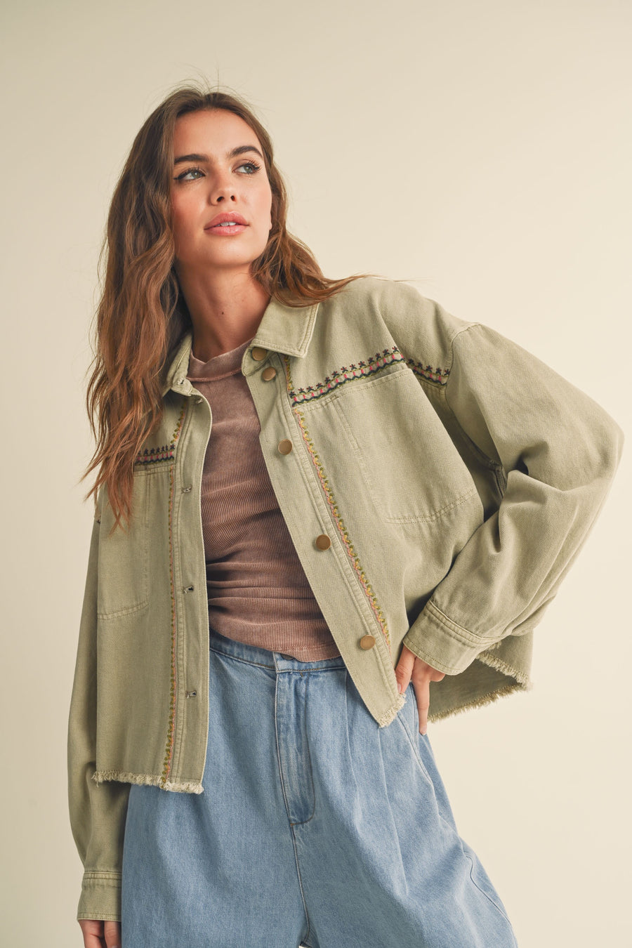 Featuring a cropped jacket with a frayed hem and colorful sitching on the front and back in the shade washed olive 