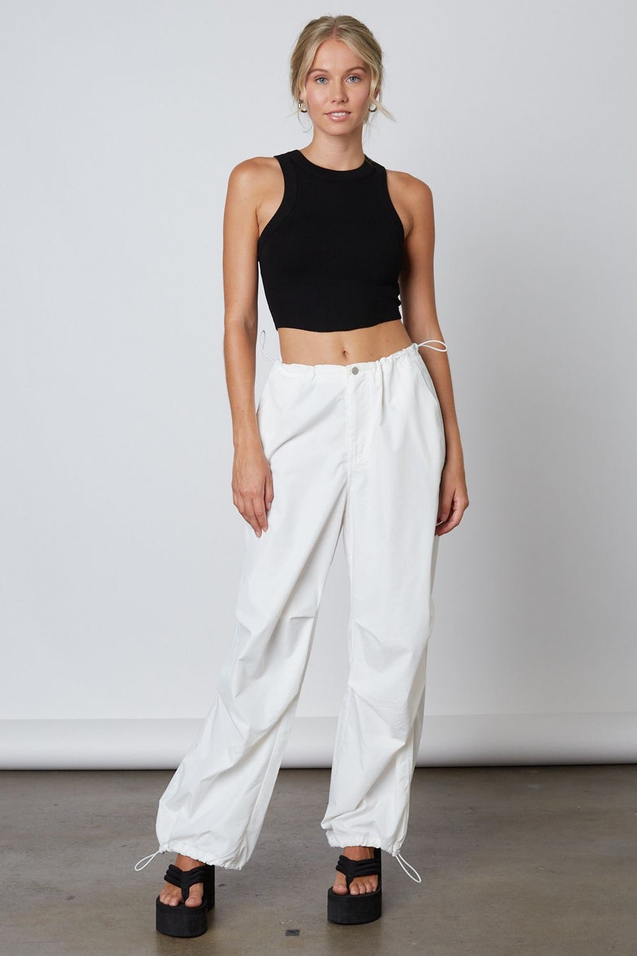 White parachute style pants with a zipper and button in front. Draw Strings that synch on the left side as well as on the bottom of the two pant leg ends.  