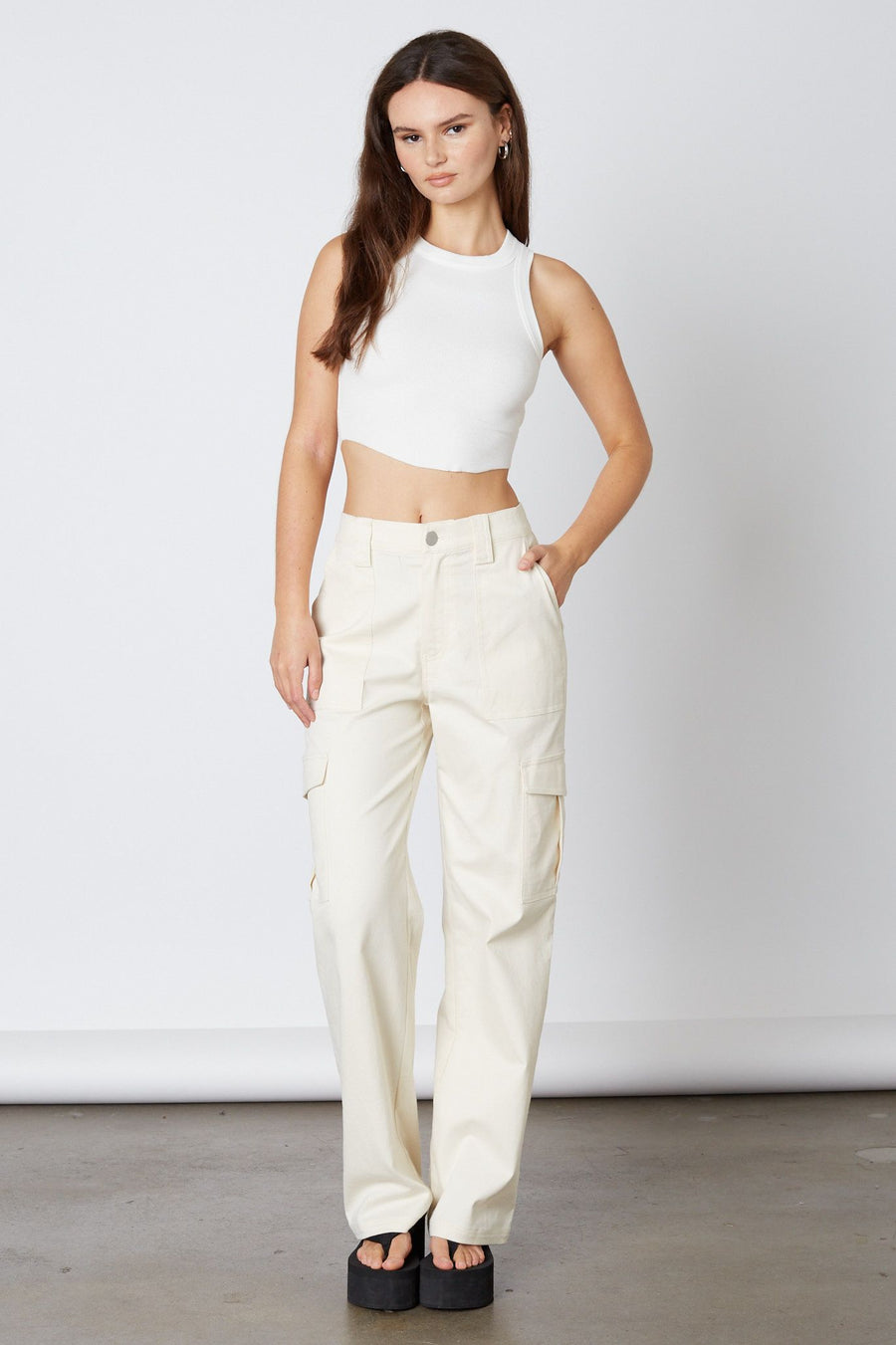 Model is wearing a white tank top with ivory cargo pants and platform flip flops.